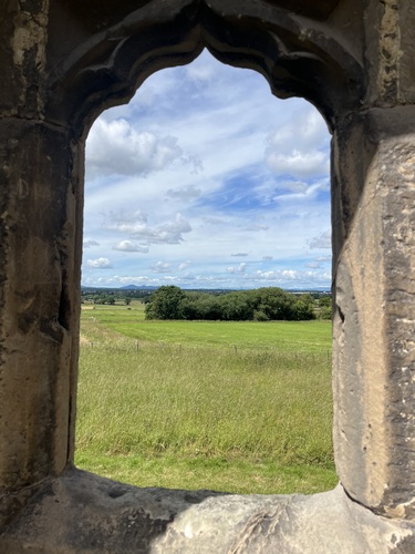 Green fields and distant hills framed by a carved stone window opening at Haughmond Abbey