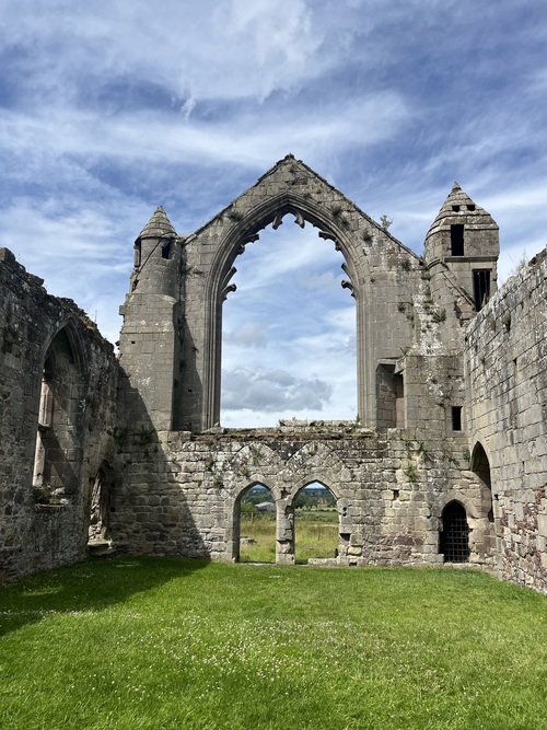 Interior view of Haughmond Abbey ruins, looking up through a tall Gothic arch flanked by two small turrets with different designs