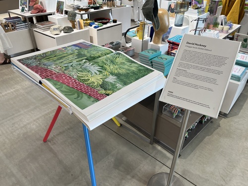 The David Hockney SUMO book open on a display stand in the Turner Contemporary gift shop, showing a large double-page spread of a lush garden painting