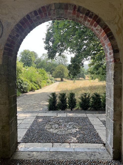 View through a brick archway in the summer house across a pebble courtyard to a gravel path and parkland beyond