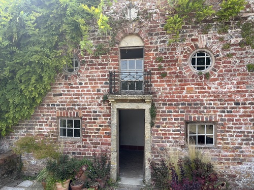 Brick exterior of the Wendy House with round windows, wisteria and potted plants by the door