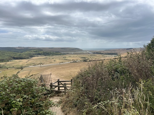 A wooden gate at a stile, looking down over the valley towards the sea