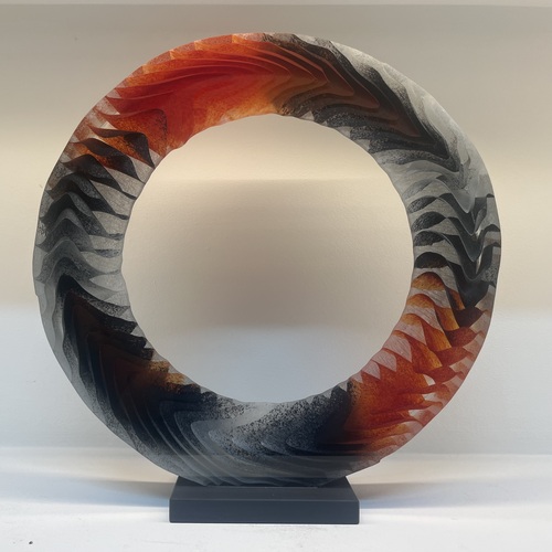 Ring-shaped glass sculpture with textured, feathered surface in grey, black and fiery orange
