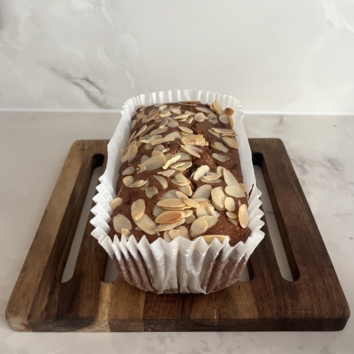 Apple and cinnamon almond-oat loaf topped with flaked almonds, in its paper liner on a wooden board