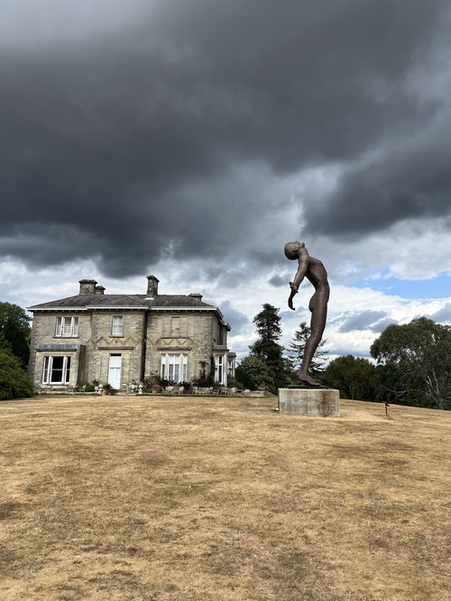 Storm clouds gathering over the house at Leonardslee, with a bronze figure sculpture, Faith, on the lawn