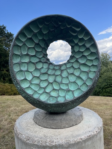 A textured bronze and resin bowl sculpture framing a circle of sky