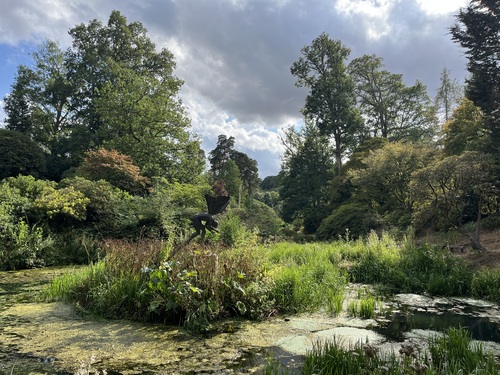 Crouching Angel: A winged bronze figure bending over the pond in the sunshine