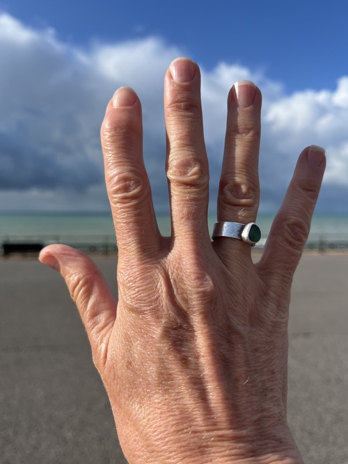 My hand raised against a stormy sky and the sea on Brighton seafront, showing the joints in my fingers and thumb