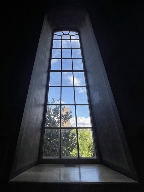 Tall arched window overlooking green trees and a tower