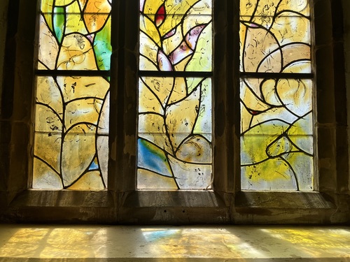 Yellow-toned stained glass panel with bird and ass, and light reflected on the sill