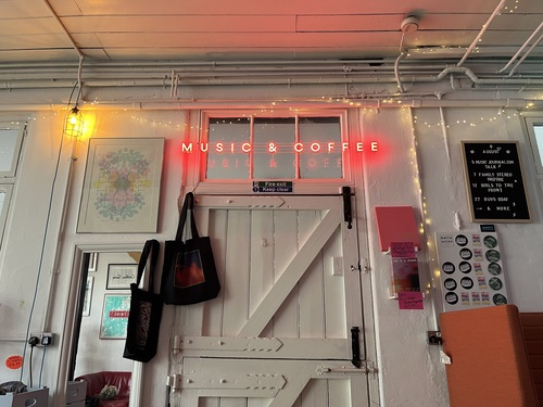 Music & Coffee neon sign above a white stable door inside Bella Union, tote bags and gig posters hanging nearby