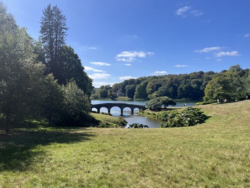 Stone bridge crossing the Stourhead lake, with the domed Pantheon visible among trees on the far bank