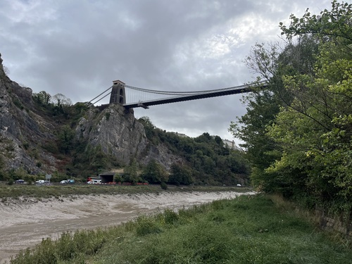 Clifton Suspension Bridge seen from below, spanning the Avon Gorge above muddy tidal flats on a grey day