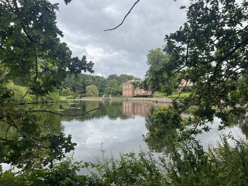 Dunham Massey's red brick house seen across the still lake, framed by overhanging oak branches