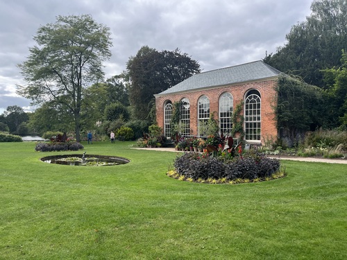 The Dunham Massey orangery, a brick building with tall arched windows, seen from the lawn with a lily pond in front