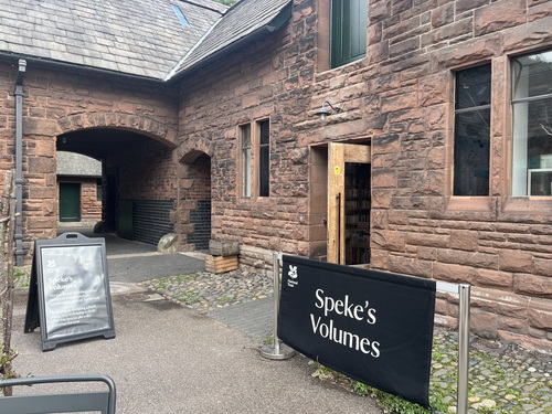 Sandstone entrance to Speke's Volumes secondhand bookshop, with a black National Trust banner and books visible through the open door