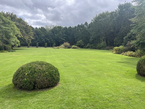 A wide lawn bordered by mature trees and flower beds in the grounds of Speke Hall