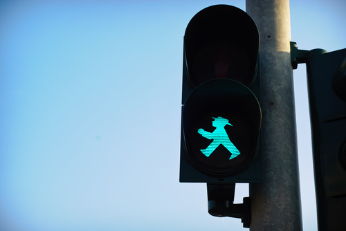 A pedestrian crossing light in Berlin showing a green walking man in a hat, against a clear blue sky
