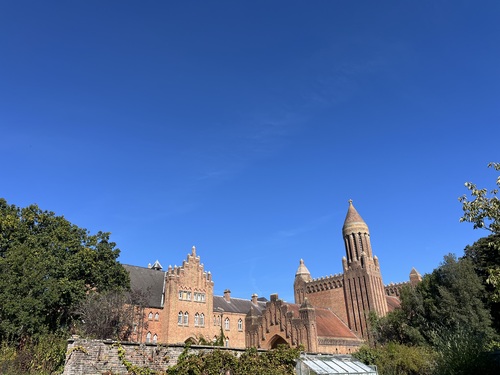 Quarr Abbey's stepped gables and tall brick tower against a deep blue sky, seen over a garden wall and greenhouse
