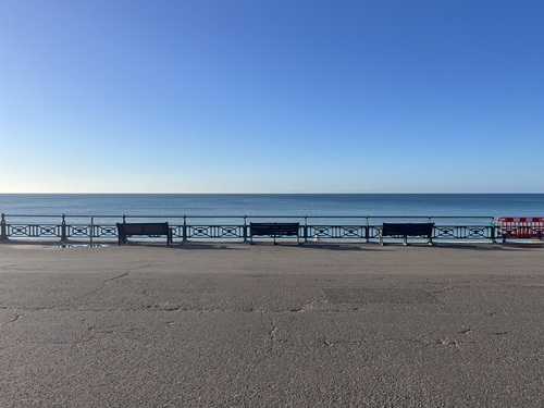 Empty seafront benches and railings on Hove promenade under a clear blue sky, before the parkrun runners arrive