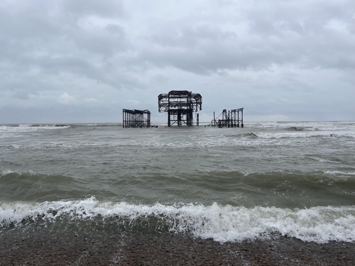 Brighton's West Pier ironwork standing in rough grey sea under heavy cloud, a tall central section flanked by two lower ones, looking more symmetrical than before