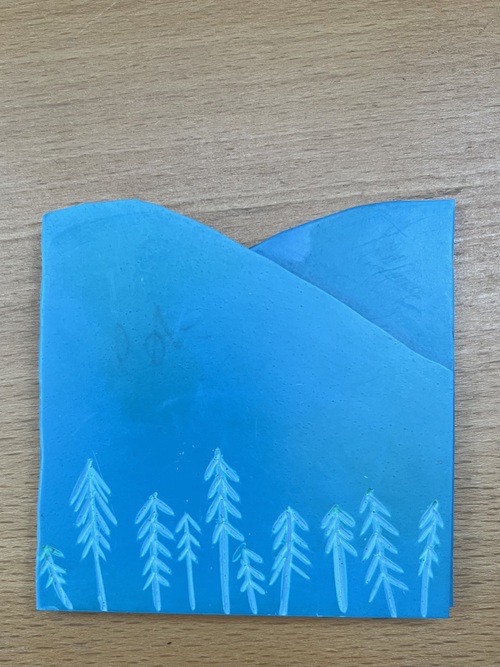 Two overlaid pieces of blue lino representing a landscape. The front one has trees carved into it and the back is solid. Both have had the sky cut away